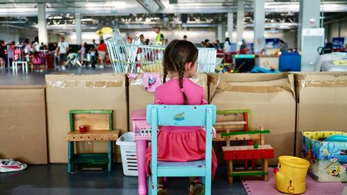 A young Ukrainian girl sits at a toy piano in a play area inside a Red Cross distribution centre in Opole, Poland, while her family collects items—such as clothes, food and toys—that they need.