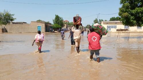 Chad Red Cross volunteers help flood-affected communities carry their possessions through flood water.