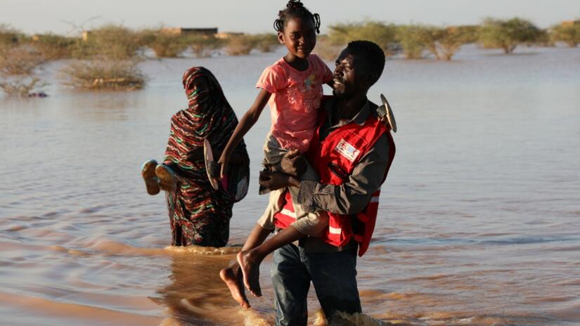 Un voluntario de la Media Luna Roja de Sudán lleva a una niña a un lugar seguro a través del agua de la inundación en el estado del río Nilo, Sudán, en agosto de 2020