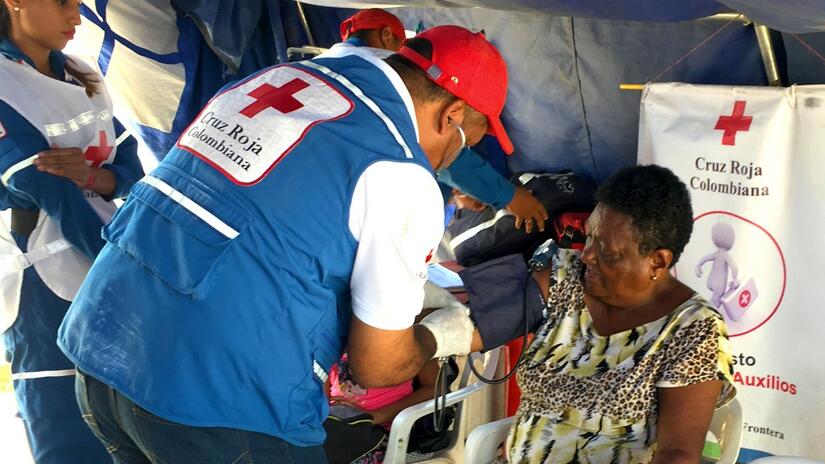 Voluntarios y voluntarias de la Cruz Roja Colombiana en un puesto de primeros auxilios temporal en La Guajira realizan un chequeo de salud a una mujer que recientemente migró al país en busca de una vida mejor