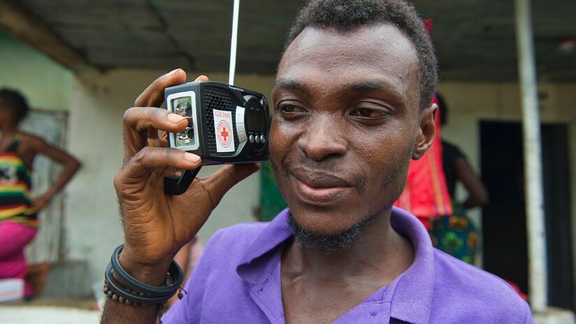 A man listens to a Red Cross broadcast on a cranking radio donated by the Sierra Leone Red Cross Society.