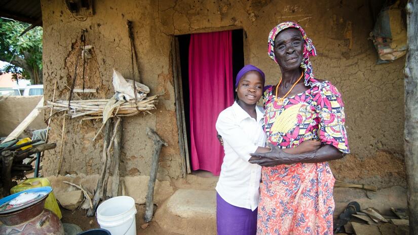 Une fille se tient avec sa grand-mère devant sa maison rurale au Nigeria.