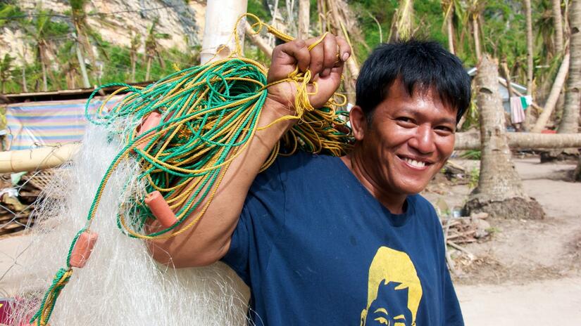 صياد في جزيرة غيغانتس نورتي في الفلبين يبتسم وهو يمسك بشبكة الصيد الخاصة به