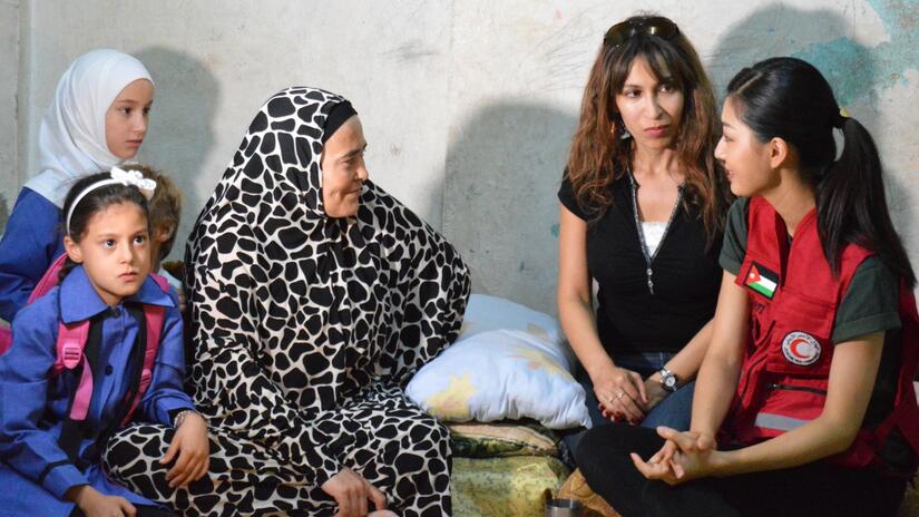 A Jordanian Red Crescent volunteer sits and talks with a family in their home