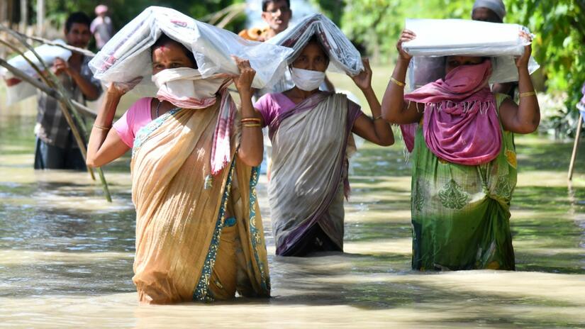 Women wade through flood waters in Assam, India in August 2020 carrying tarpaulins provided by the Indian Red Cross Society following devastating monsoon flooding