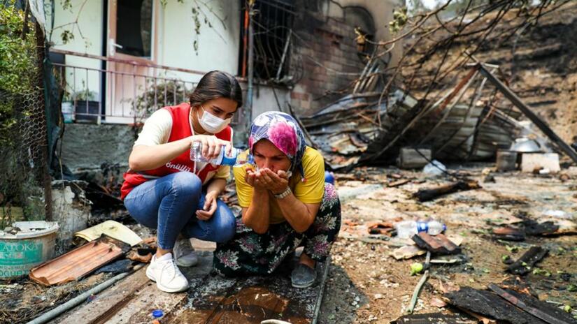 متطوّعة من الهلال الأحمر التركي تساند امرأة تضررت من حرائق الغابات في آب/أغسطس 2021، وتزودها بالمياه النظيفة وتساعدها في ترتيب المأوى فضلاً عن تقديم الدعم النفسي والإجتماعي