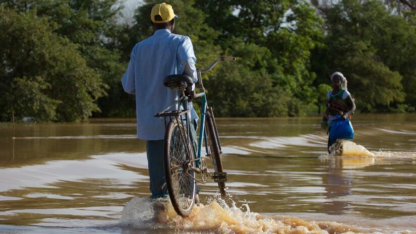 A man carries his bike through flood water in Burkina Faso. Climate change in the Sahel region has made the rains more erratic and led to localized flooding and droughts.