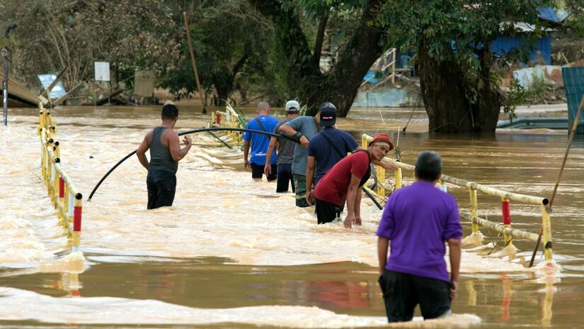 People in Terengganu, Malaysia try to cross a bridge to their homes that was submerged by devastating floods in early 2021.