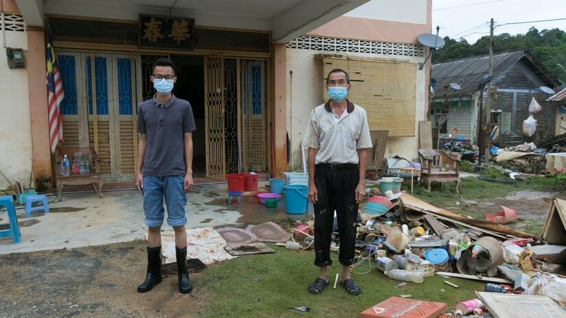 Two homeowners in Malaysia stand next to destroyed furniture and belongings following severe flooding in summer 2021