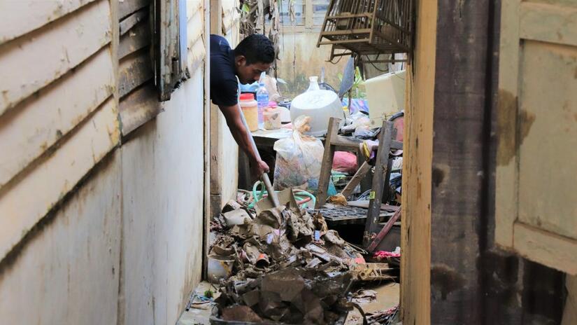 A man in Terngganu, Malaysia shovels waste out of his house which was badly damaged by flooding in summer 2021