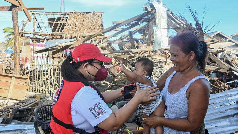 A Philippine Red Cross volunteer provides welfare support to a mother and child in an area devastated by Super Typhoon Rai in the eastern Philippines
