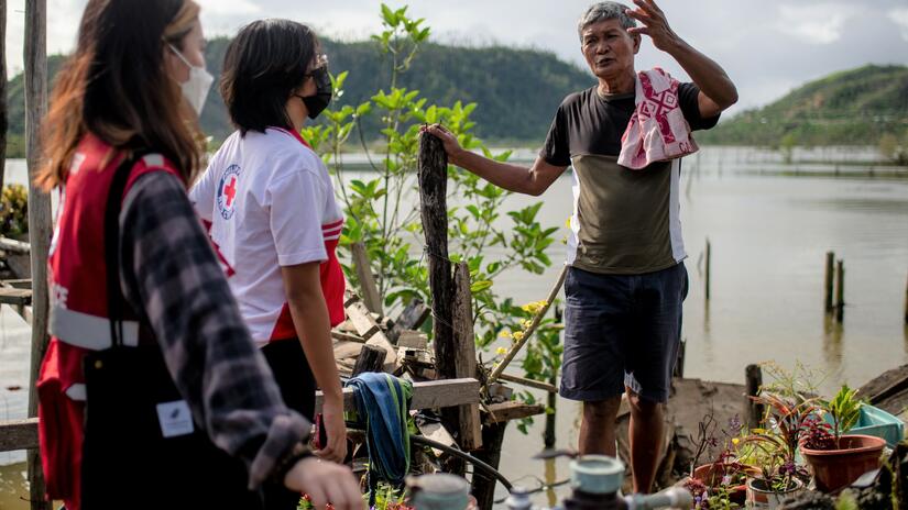 A Filipino man stand amongst what's left of his home after Typhoon Rai ruined it. He shares his troubles with Philippine Red Cross Volunteers.