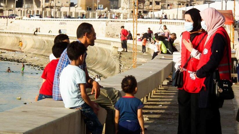 Two Libyan Red Crescent volunteers speak to a father and his children about how to stay safe from COVID-19 and let them know why and how to get vaccinated