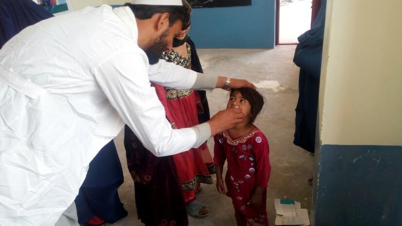 Un voluntario de la Media Luna Roja Afgana administra una vacuna oral contra la poliomielitis a una niña pequeña como parte de su campaña de inmunización.