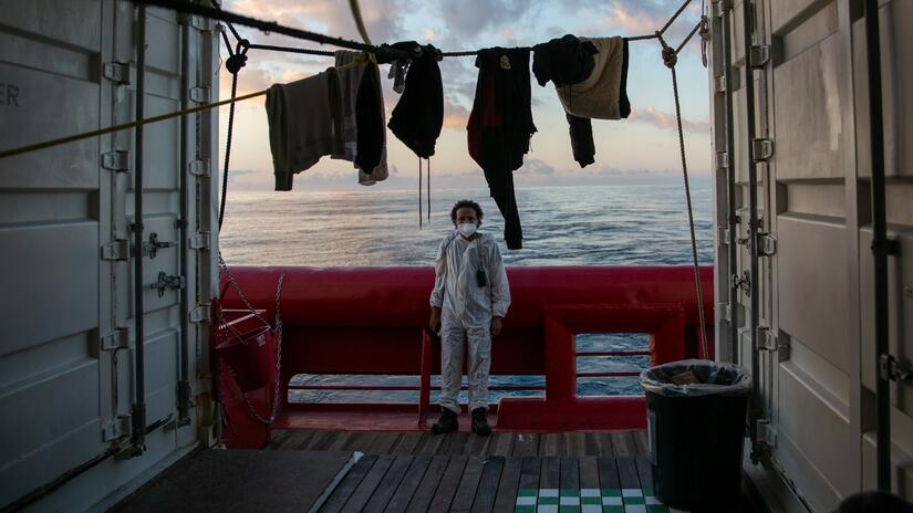 Abdel aboard the rescue ship Ocean Viking at dusk, wearing personal protective equipment, as he waits to help rescued people at sea.