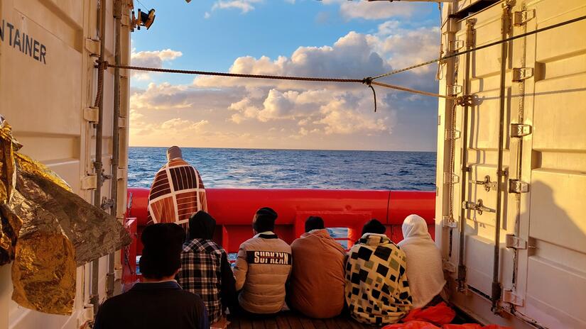 Las personas rescatadas en el mar se sientan juntas a bordo del barco de rescate Ocean Viking en febrero de 2022, mientras la tripulación del barco espera que se les asigne un lugar seguro para desembarcar a los supervivientes.