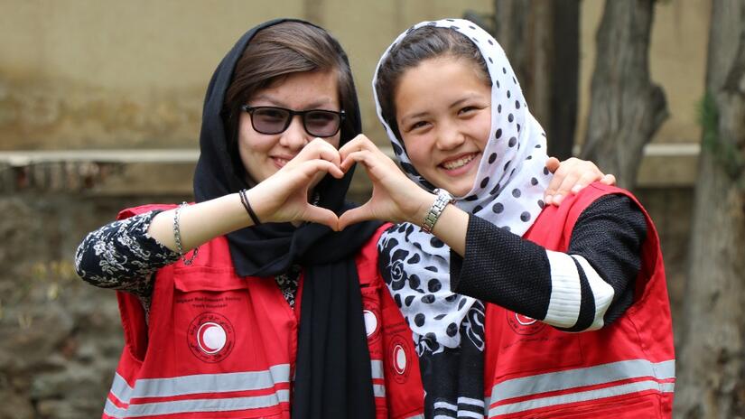 Two female Afghan Red Crescent Society volunteers put their hands together to form the shape of a heart