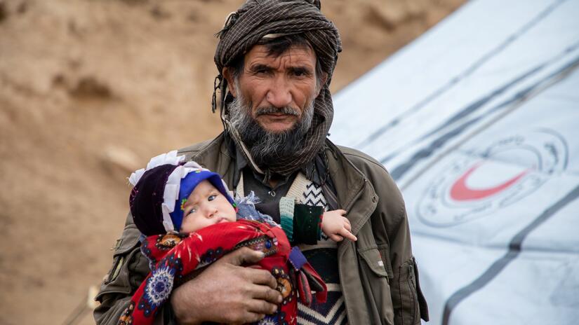 An Afghan man holds his child as awaits food aid and cash assistance to help feed his family.