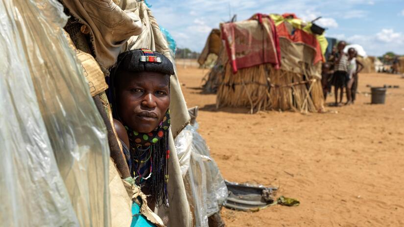 A woman from the Mucawana tribe in southern Angola peers out of her shelter home in Etunda refugee camp, Namibia, in May 2022. Drought had caused her crops to fail and livestock to die out, prompting her and her family to make the long trek to Namibia in search of food and water.