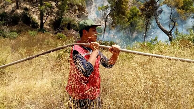 A volunteer from the Tunisian Red Crescent carries a hosepipe to help fight wildfires in Tunisia in August 2021.