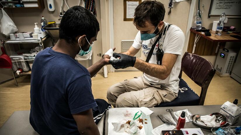 A crew member on board the Ocean Viking rescue ship tends to the wounds of a young man rescued in the Central Mediterranean in August 2022