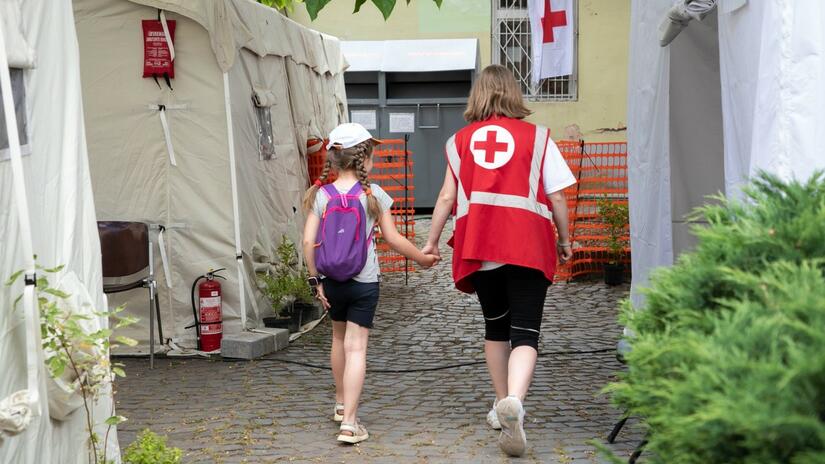 A young girl walks hand in hand with a Red Cross volunteer in Uzhhorod, Ukraine. The Red Cross Health Centre there offers consultation, treatment and medication free of charge for people in need. It’s open to everyone, the local community and internally displaced people alike.