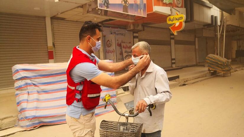 Un voluntario de la Media Luna Roja iraquí ayuda a un hombre a ponerse una mascarilla protectora durante una fuerte tormenta de arena en el país en 2022.