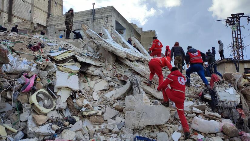 متطوعو الهلال الأحمر العربي السوري يهرعون لإنقاذ الأشخاص المحاصرين تحت المباني المنهارة في اللاذقية في أعقاب الزلازل المدمرة في 6 فبراير/شباط 2023. 