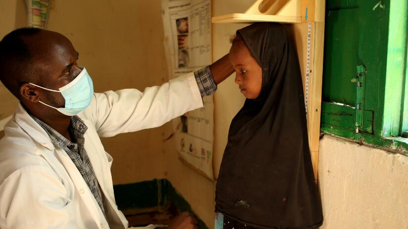 4-year-old Mardiye stands tall to have her height measured in by nutrition nurse Hersi Adan Yasin at a health clinic operated by the Somali Red Crescent Society.