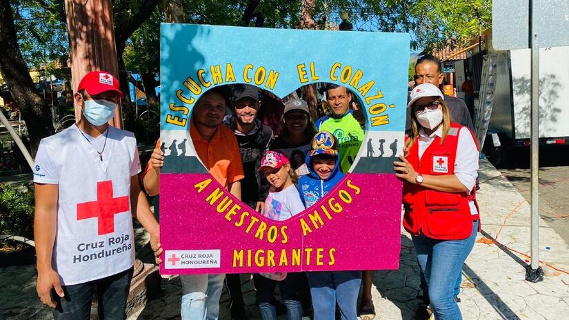 Honduran Red Cross volunteers hold up a sign saying 'listen with heart to our migrant friends' during a health fair for people on the move through Honduras in December 2022.