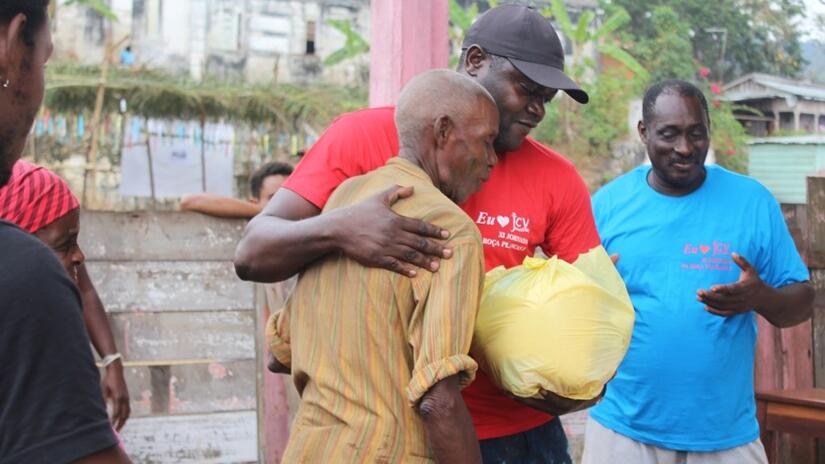 Cristiano, responsable de la communication de la Croix-Rouge de São Tomé et Príncipe, étreint un homme âgé et lui donne un sac de produits alimentaires lors d'un événement communautaire en 2019.