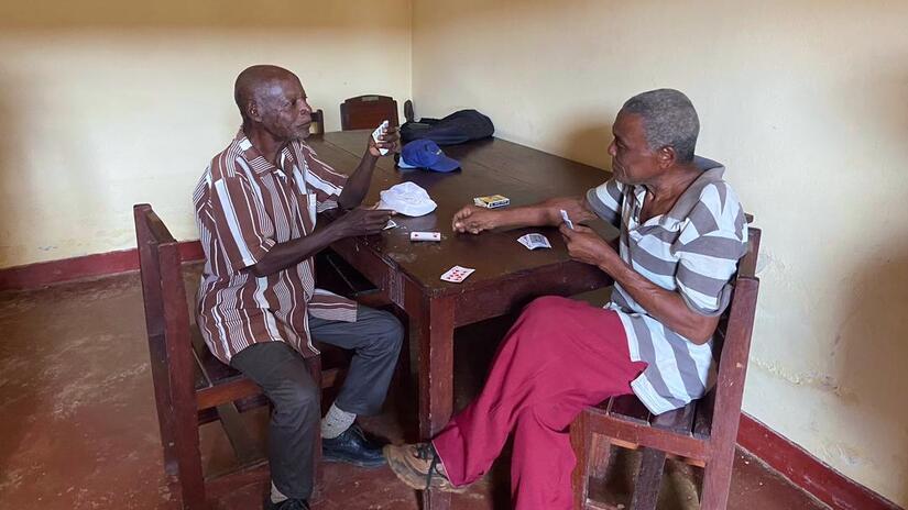 Two men sit at a table together playing cards in a social centre run by the São Tomé and Príncipe Red Cross.
