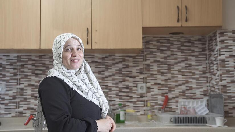 Houda smiling to the camera while standing in her happy place, the kitchen