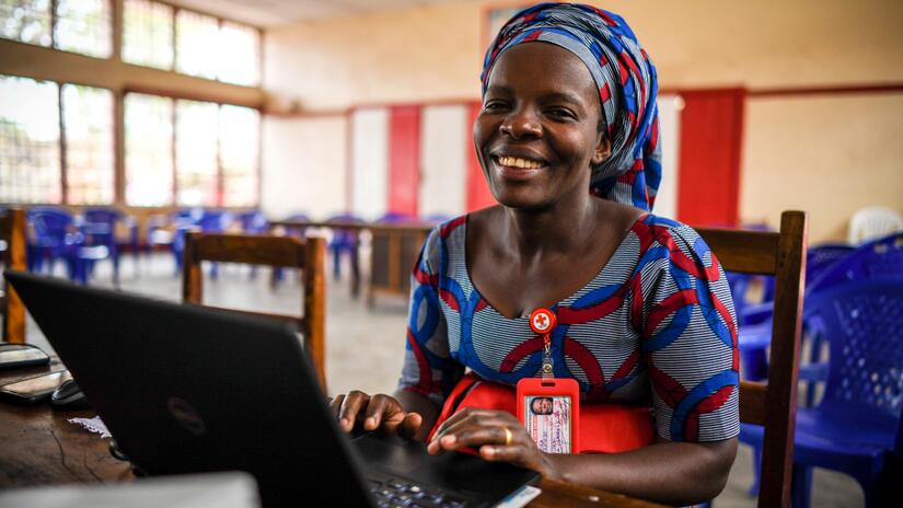 A staff member for the Democratic Republic of the Congo Red Cross works on her computer and smiles.