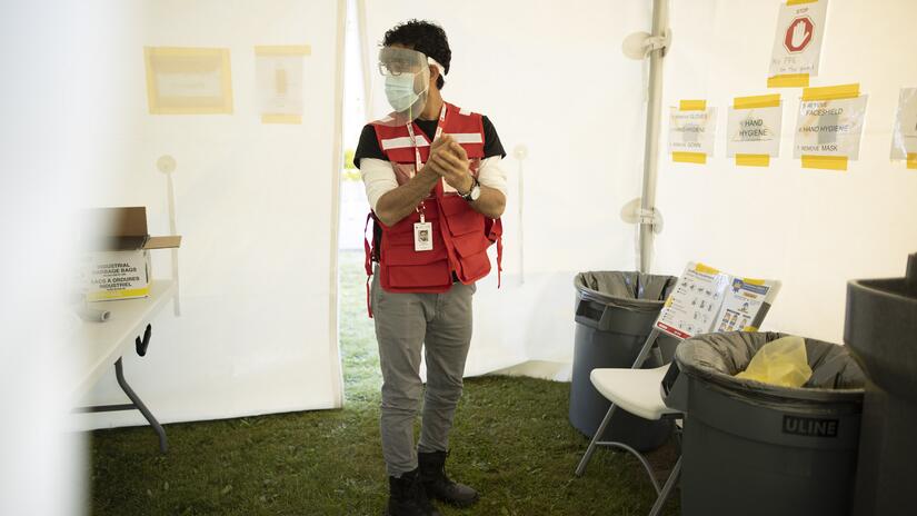 يرتدي حسن سترة الصليب الأحمر الكندي ويطهّر يديه أثناء عمله في موقع تلقيح واختبار فيروس كورونا. 