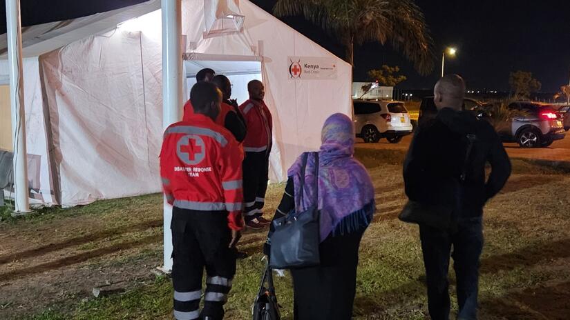 A man and woman who fled conflict in Sudan are guided towards a tent run by the Kenya Red Cross in Nairobi where they can access mental health support.