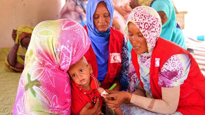 Voluntarias de la Media Luna Roja Mauritana miden la circunferencia del brazo de un niño pequeño en junio de 2023 para comprobar si está desnutrido.