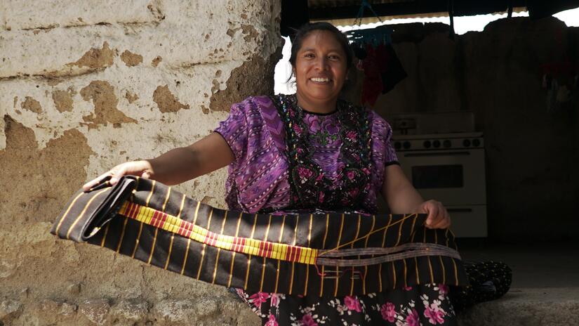 Gladis holds up a corte - a traditional Mayan skirt - she is weaving which features a yellow striped band, representing hope.