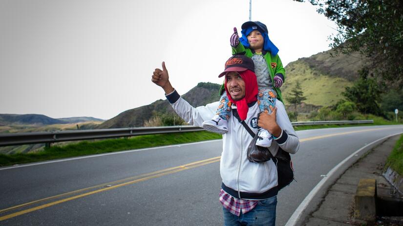 Little Santiago sticks his thumb out to try and catch the attention of passing traffic so he and his dad can hitch a ride.