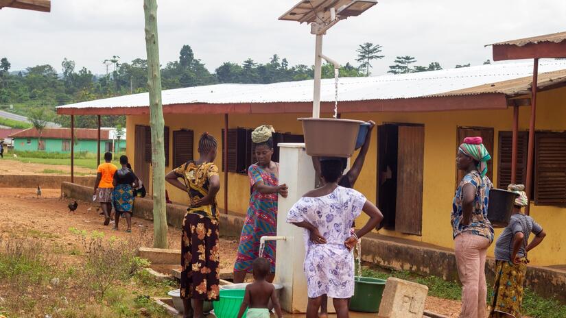 Joyce y personas vecinas de su comunidad recogen agua de la bomba solar situada en el corazón de su aldea.
