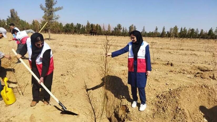 Two Iranian Red Crescent Society youth volunteers work together to plant a tree in an arid part of the country in a bid to reforest an area of land and make it more resilient to climate-related disasters.