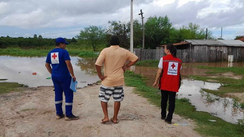 Dos personas de la Cruz Roja Paraguaya hablan con un hombre local, frente a una carretera inundada en el sector de Concepción-Marzo 2023.