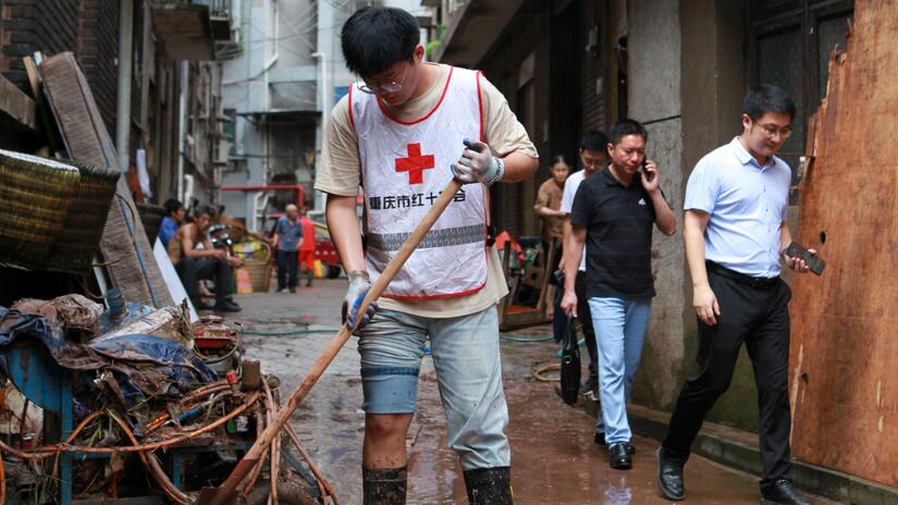 متطوع من فريق الإغاثة في حالات الكوارث التابع لجمعية الصليب الأحمر الصيني في تشونغتشينغ يقوم بتنظيف شارع متأثر بالفيضانات الشديدة في يوليو/تموز 2023. 