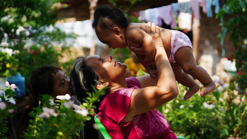 Rosa tient sa petite fille dans ses bras à l'extérieur de sa maison, dans l'ouest du Salvador, et sourit.