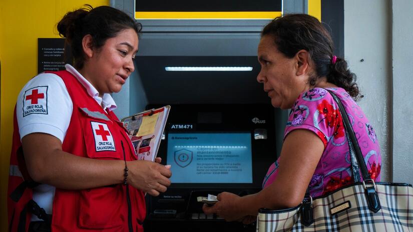 Una voluntaria de la Cruz Roja Salvadoreña ayuda a Rosa, del oeste de El Salvador, a sacar dinero de un cajero automático para ayudarla a ella y a su familia a hacer frente al terremoto de enero de 2023.