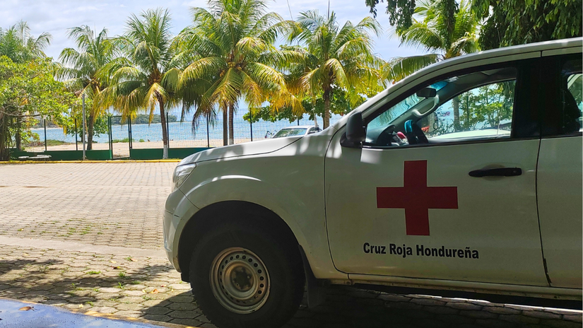 Con el mar y palmeras de fondo, un vehículo de Cruz Roja Hondureña se estaciona en el parqueo del Centro de Atención al Migrante Retornado.