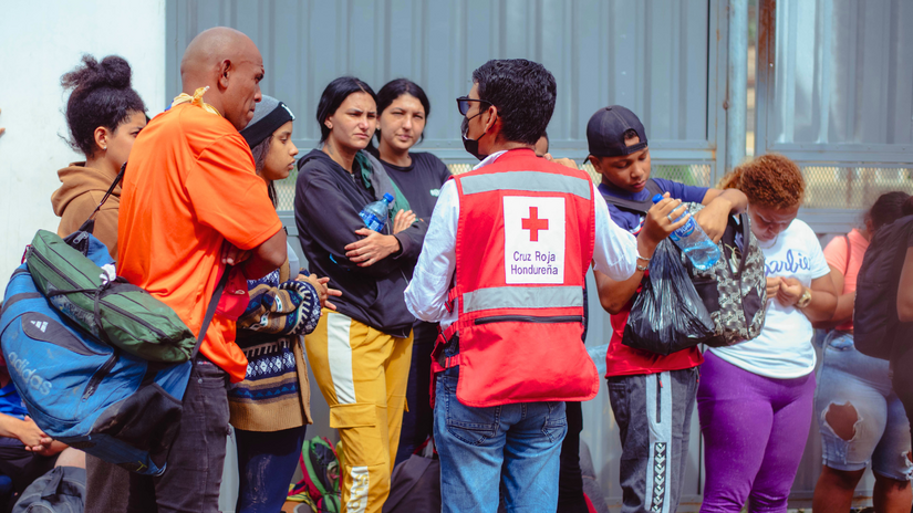Un voluntario de Cruz Roja Hondureña brinda información a personas migrantes que hacen una fila para recibir atención en múltiples servicios.
