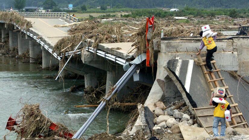 Volunteers from the Republic of Korea National Red Cross climb over a collapsed bridge to deliver humanitarian supplies. Photo: IFRC
