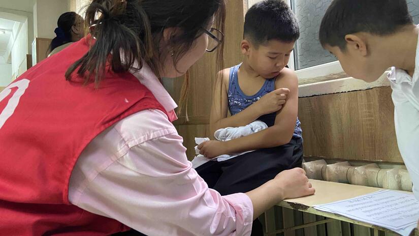 A Kyrgyzstan Red Crescent volunteer administers a measles vaccine to a young boy.