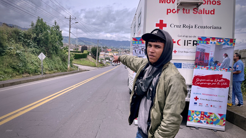 Yender stands in front of a Mobile Health Unit from Ecuadorian Red Cross, pointing to the long road that he will soon walk ahead.
